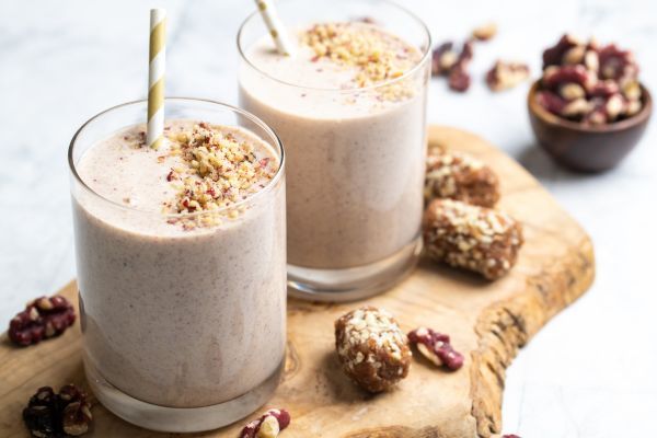 Two smoothies in glasses with toppings on a wooden board.