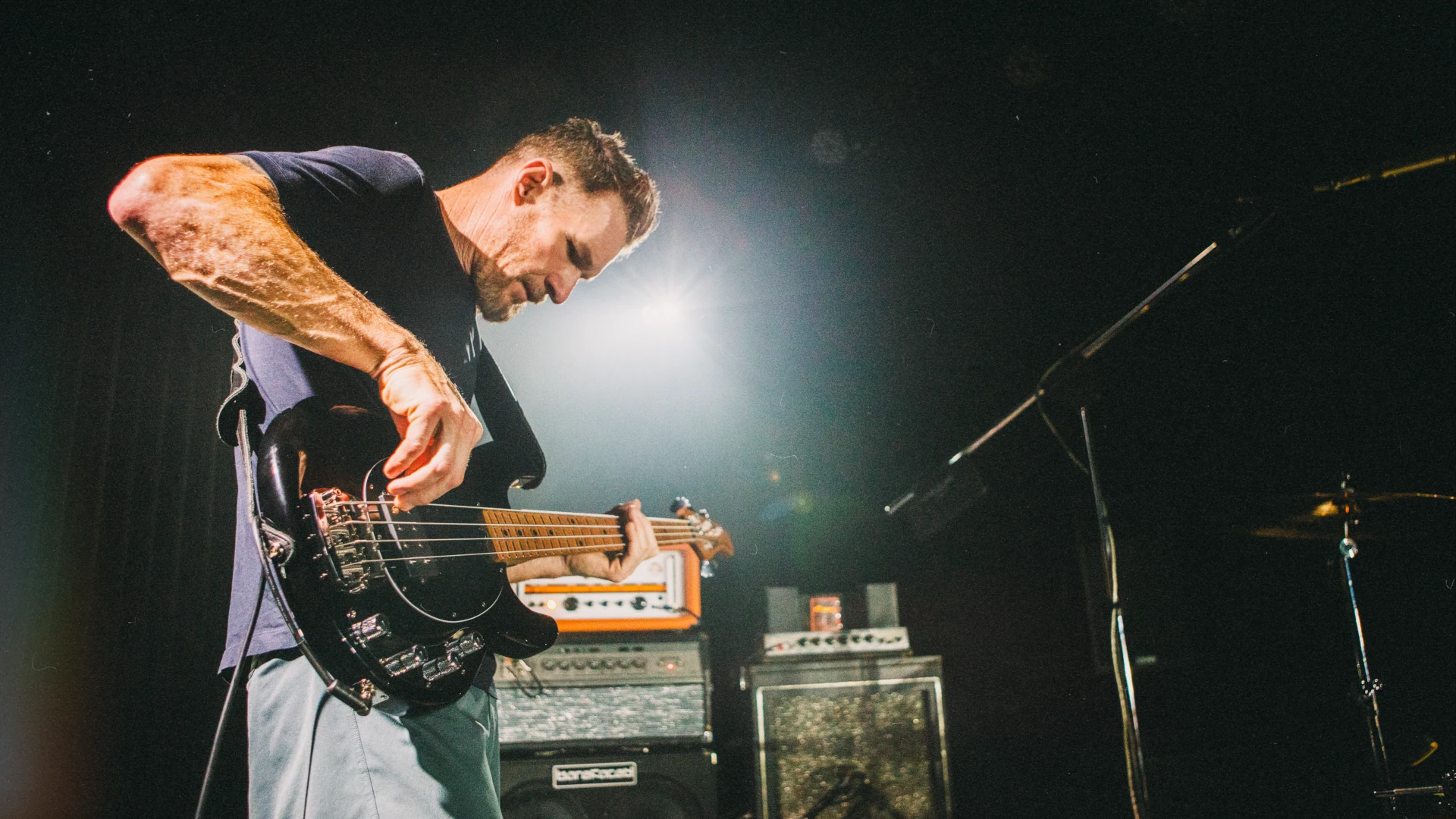 Tim Commerford playing bass guitar on stage with vibrant lighting.