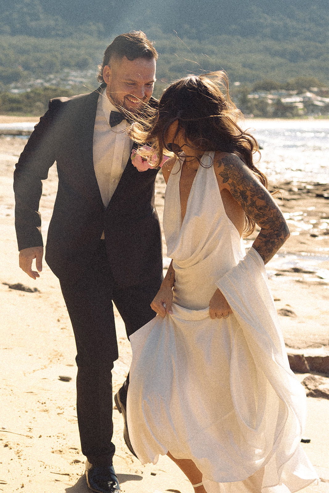 Couple in formal attire walking joyfully on a beach.