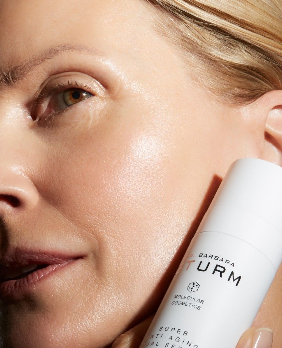 Close-up of a woman holding a skincare product, showcasing her glowing skin.