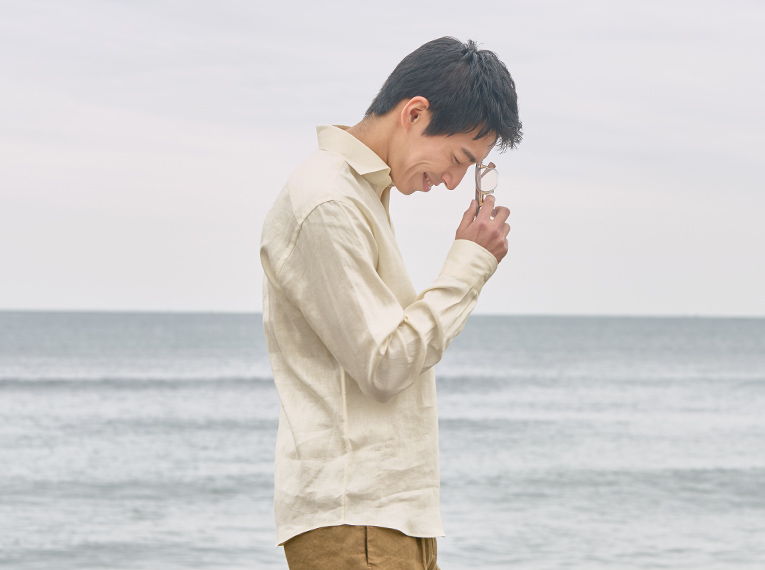 A young man standing by the ocean, looking down thoughtfully.