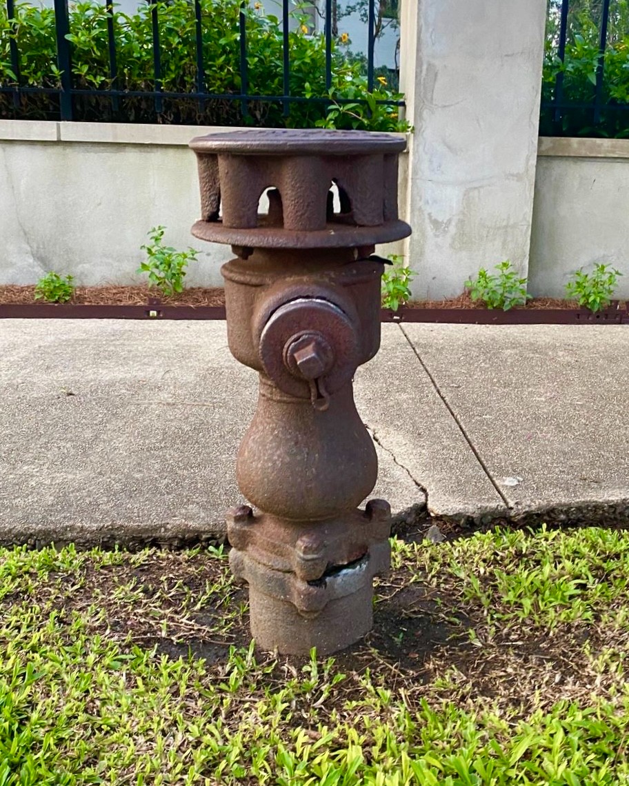 Rusty fire hydrant on a concrete sidewalk with grass nearby.