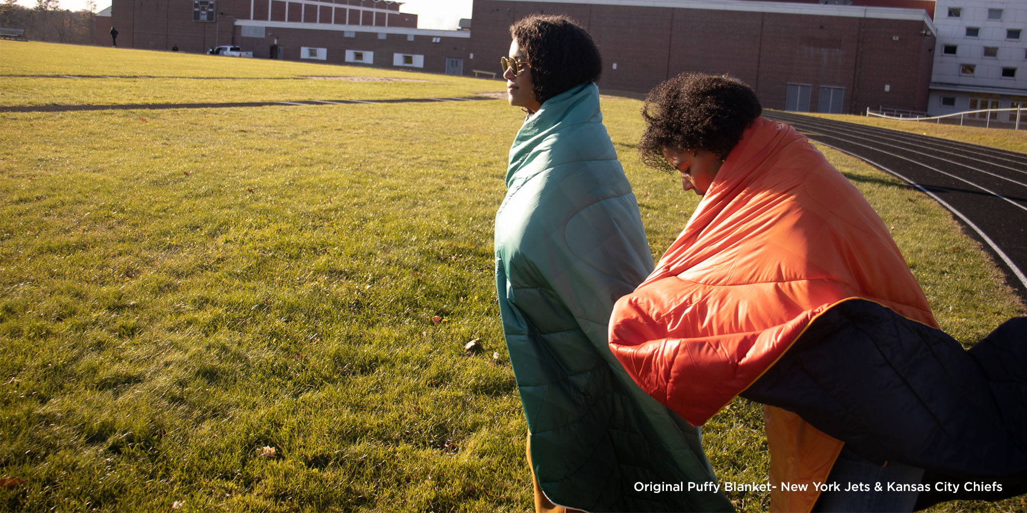 Two people wearing NFL Rumpl blankets on field