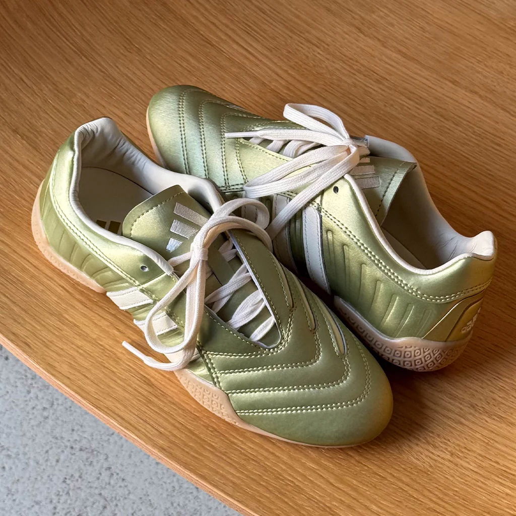 Green athletic shoes with white stripes on a wooden surface.