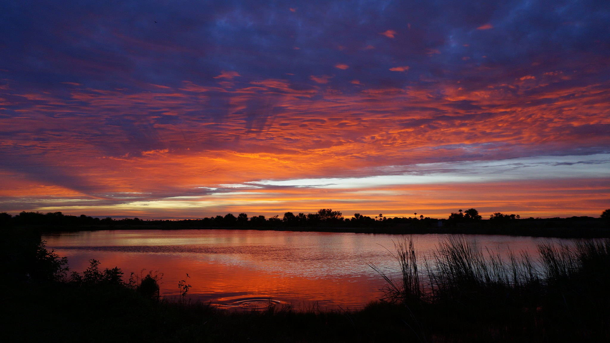 Orange, purple, and blue colors fade into the clouds as the sun sets over a lake.