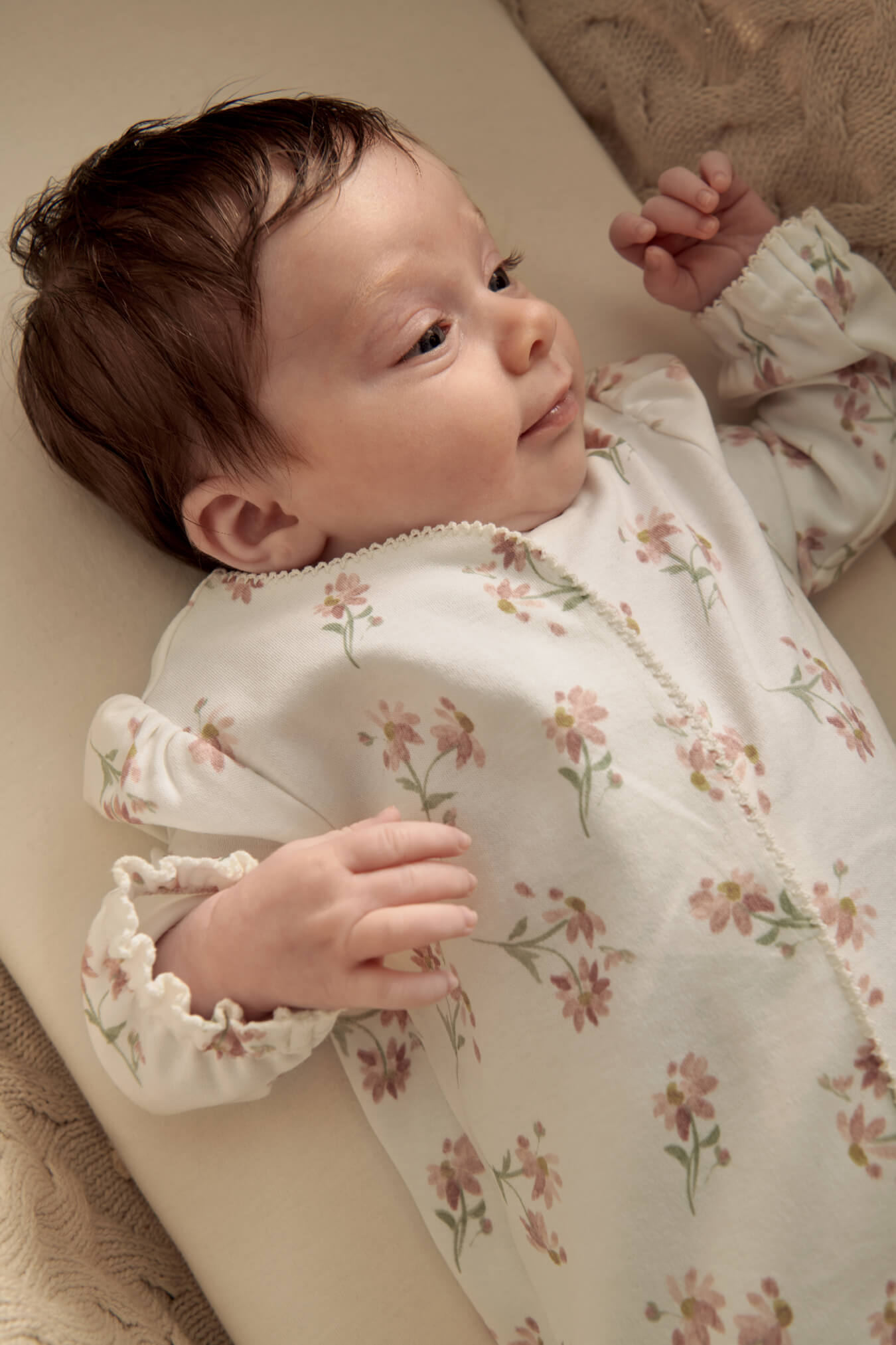 Baby lying on a surface, wearing a floral-patterned onesie.