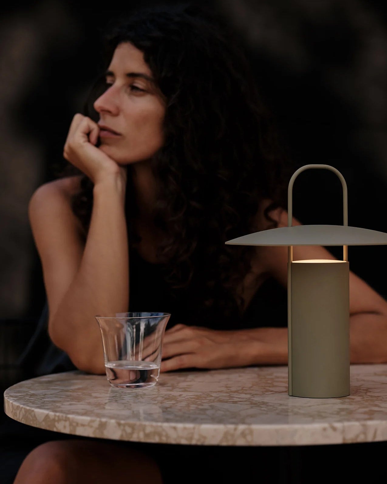 Woman sitting at a table with a glass of water and a Dusty Green table lamp.
