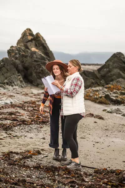 Owner Kathleen and model look at papers on the beach.