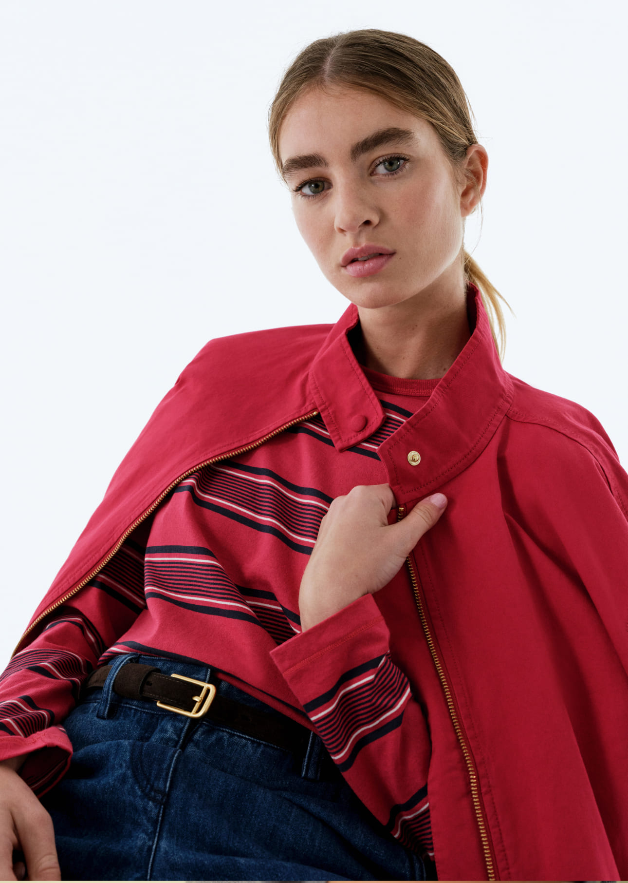 Woman wearing a red jacket over a striped shirt, looking at the camera.