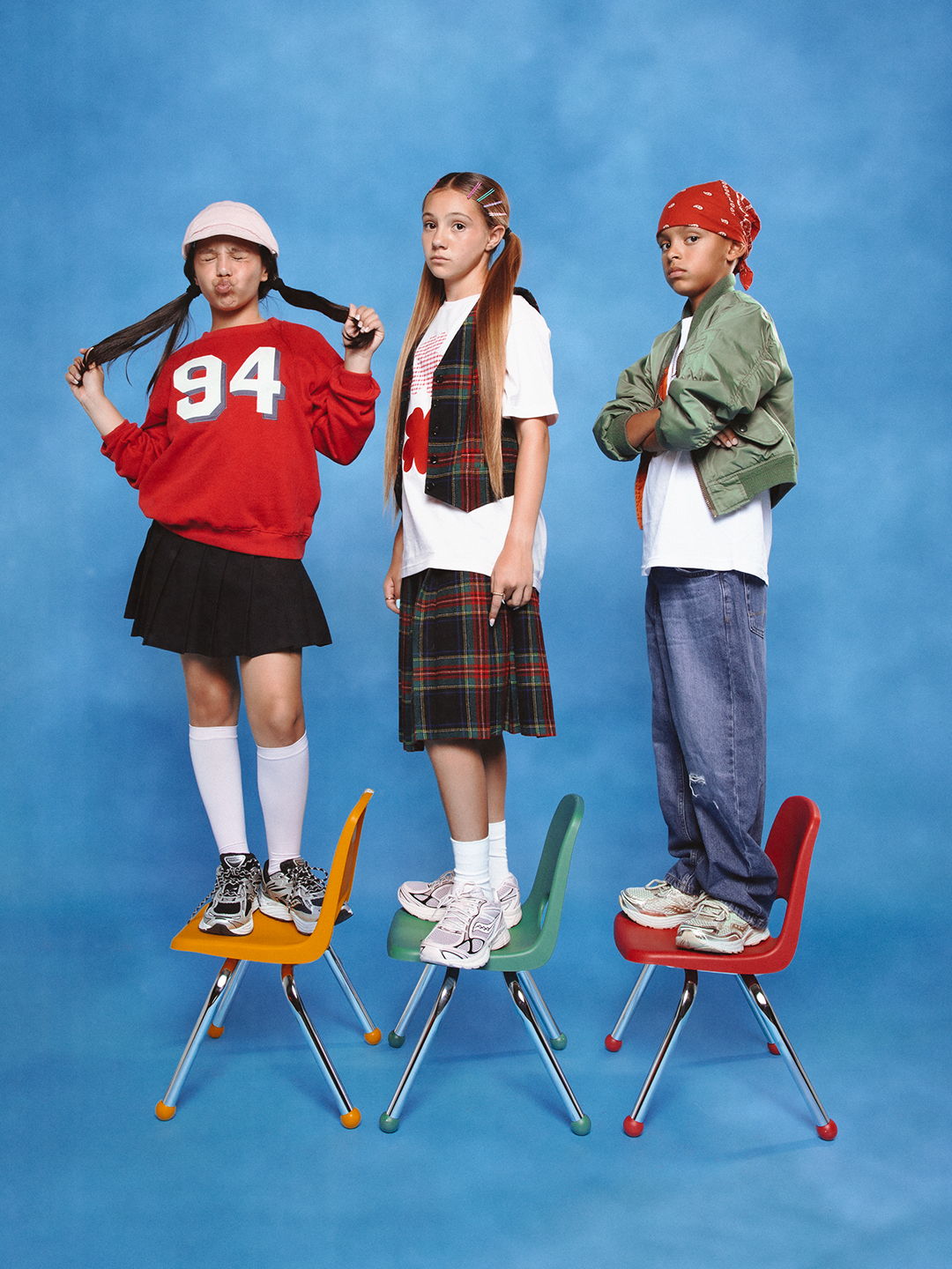 Three young people standing on colorful chairs against a blue background.