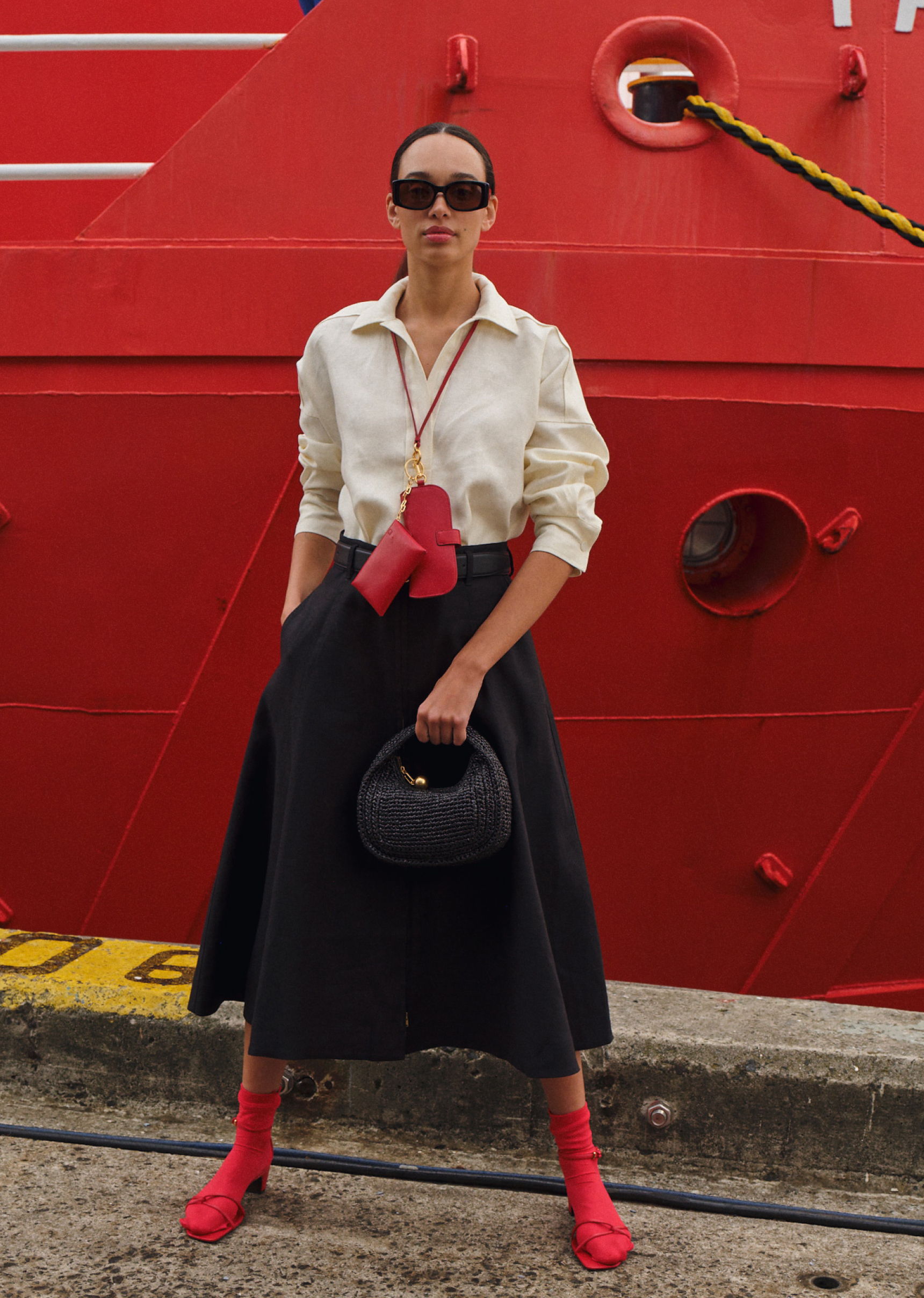 Woman in stylish outfit stands by a red ship.