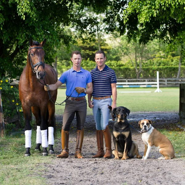 David and Nicholas Fyffe Dressage standing with a chestnut colored horse on their right, and  2 dogs, a Rotweiller and a Boxer on their left on a horse trail.