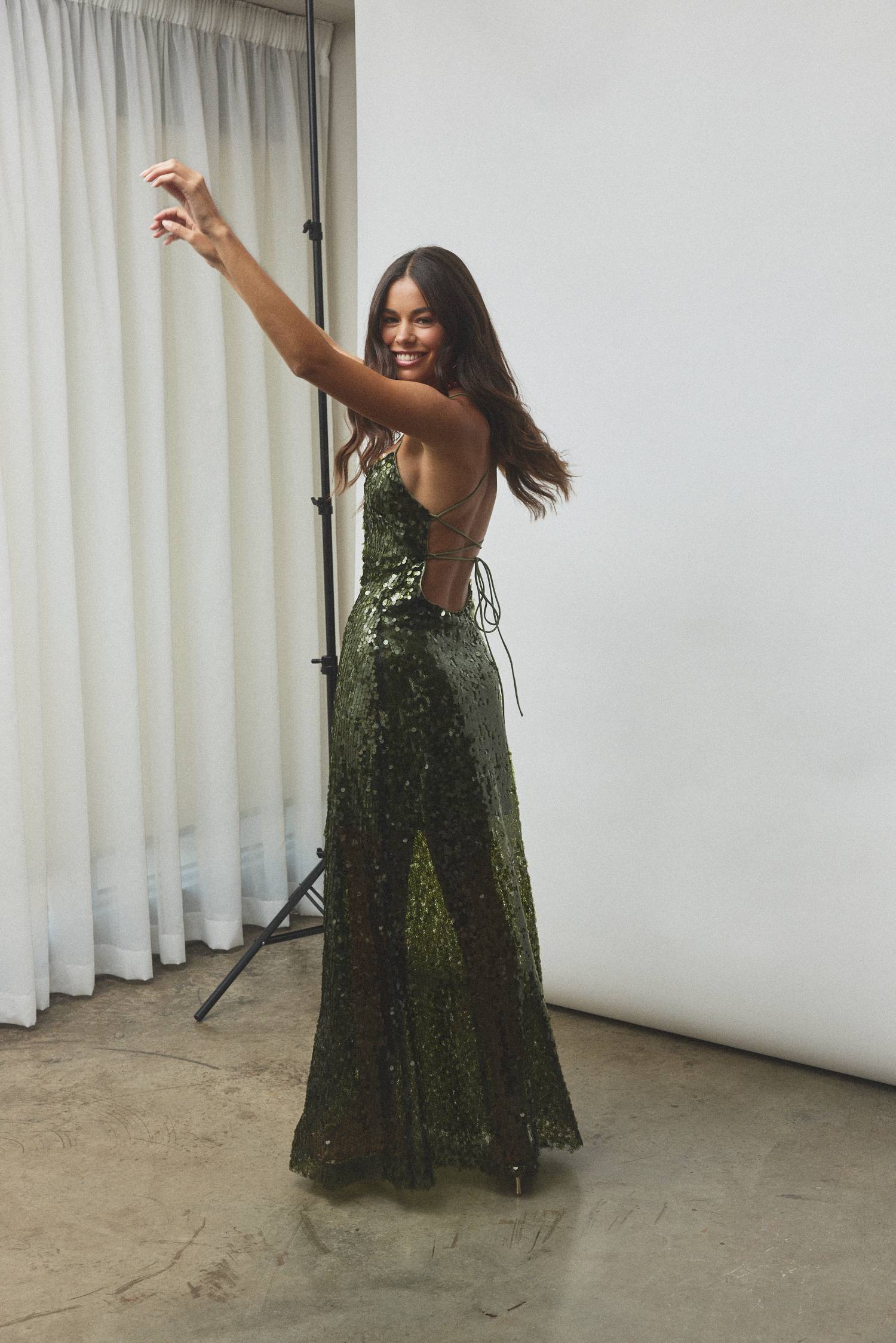 Woman in a sequined green dress posing in a studio setting.