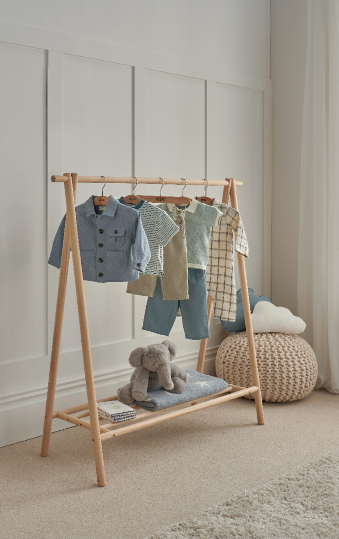 Children's clothes displayed on a wooden rack with a stuffed elephant nearby.