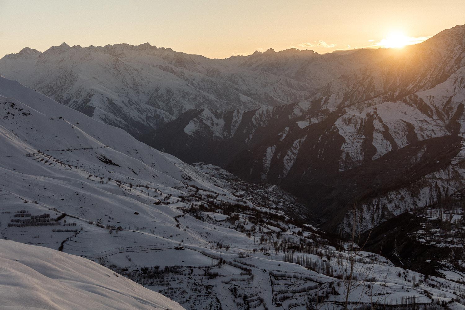 Snow-covered mountains at sunset, with a valley below.