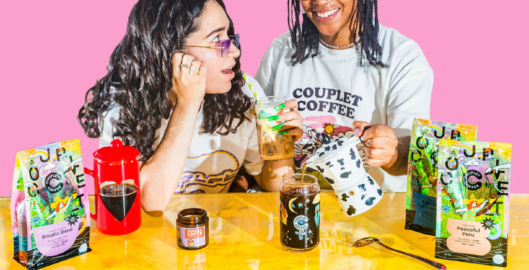 Two women enjoying coconut coffee products on a colorful table.