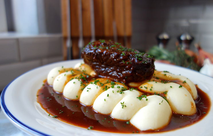 A plate of mashed potatoes with beef and brown sauce, garnished with herbs.