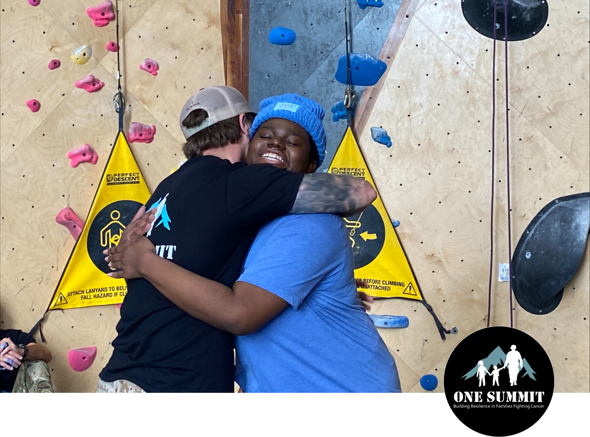Two people hugging in front of a rock climbing wall
