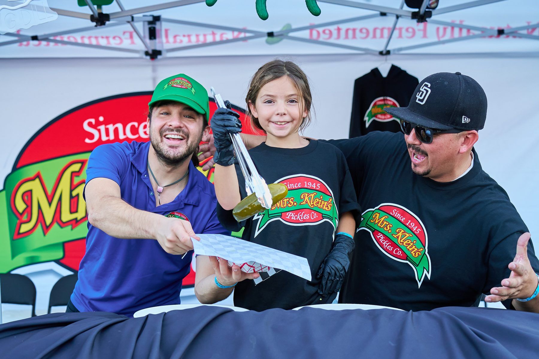 Mrs. Klein's Pickles vendors with a young guest holding a pickle with tongs at The Big Dill at Globe Life Field in Arlington Texas 2025.