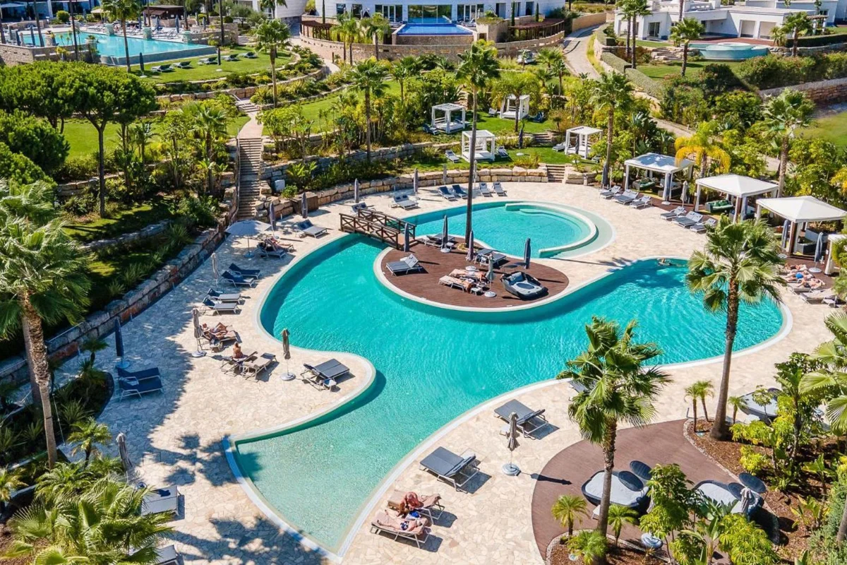 Large hotel pool deck featuring commercial chaise lounges, umbrellas, cabanas, and landscaped outdoor seating areas
