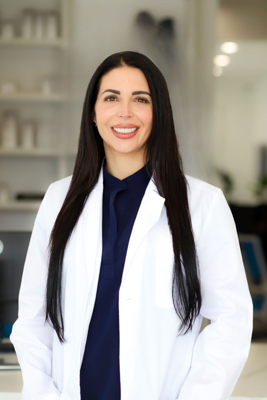 Smiling woman in a white lab coat, standing in a professional setting.