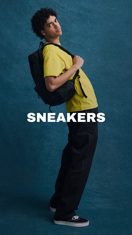 Person wearing yellow shirt and black pants, posing with a backpack. SNEAKERS.