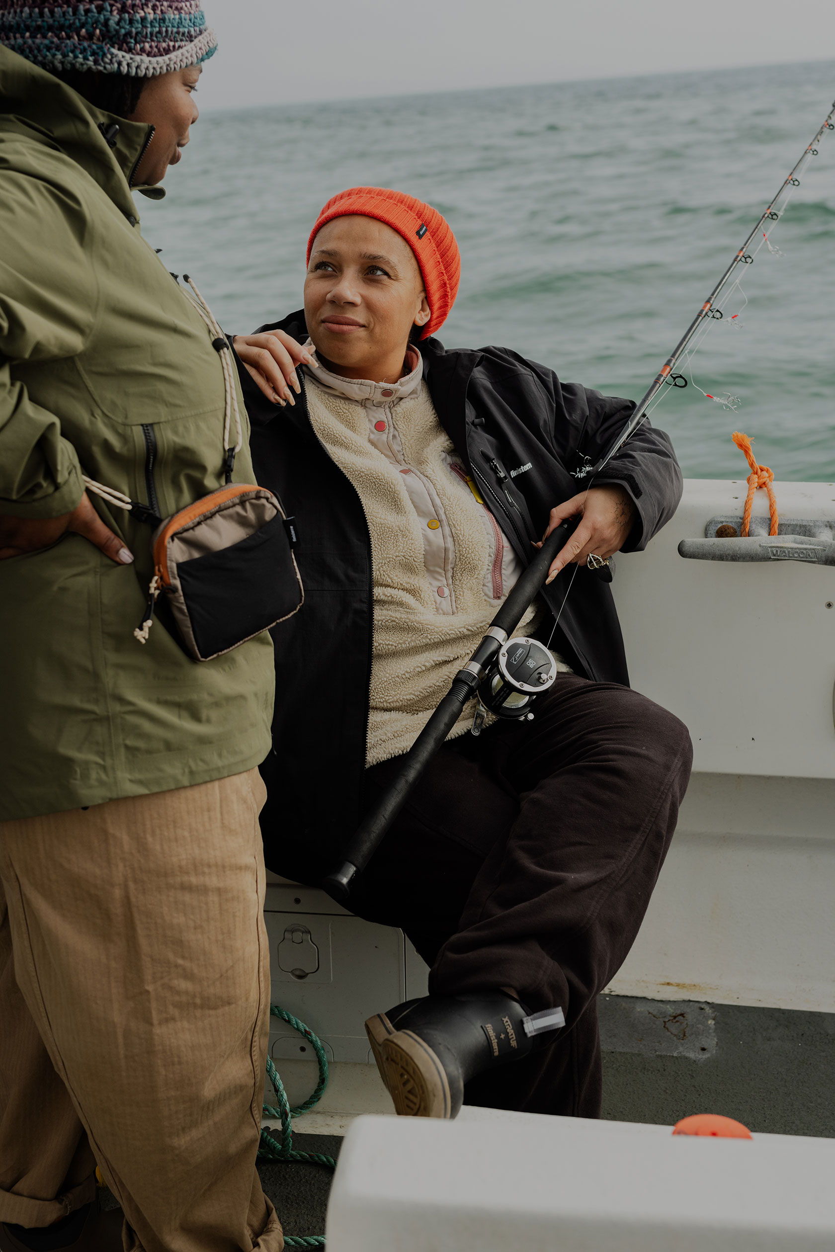 Two women fishing on a boat, one holding a fishing rod and smiling.