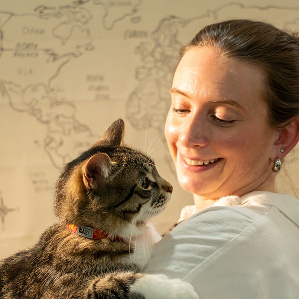 Woman smiling while holding a cat in front of a world map.