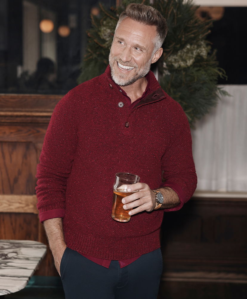 Smiling man in a red sweater holding a beer in a cozy setting.