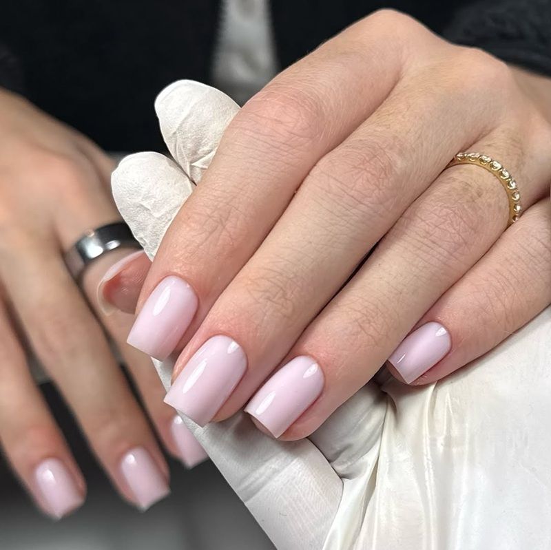 A hand with pink nails and rings, held by a gloved hand.