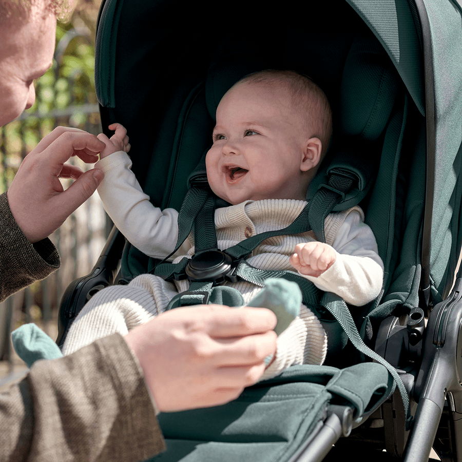 A joyful baby in a stroller interacting with a caregiver.