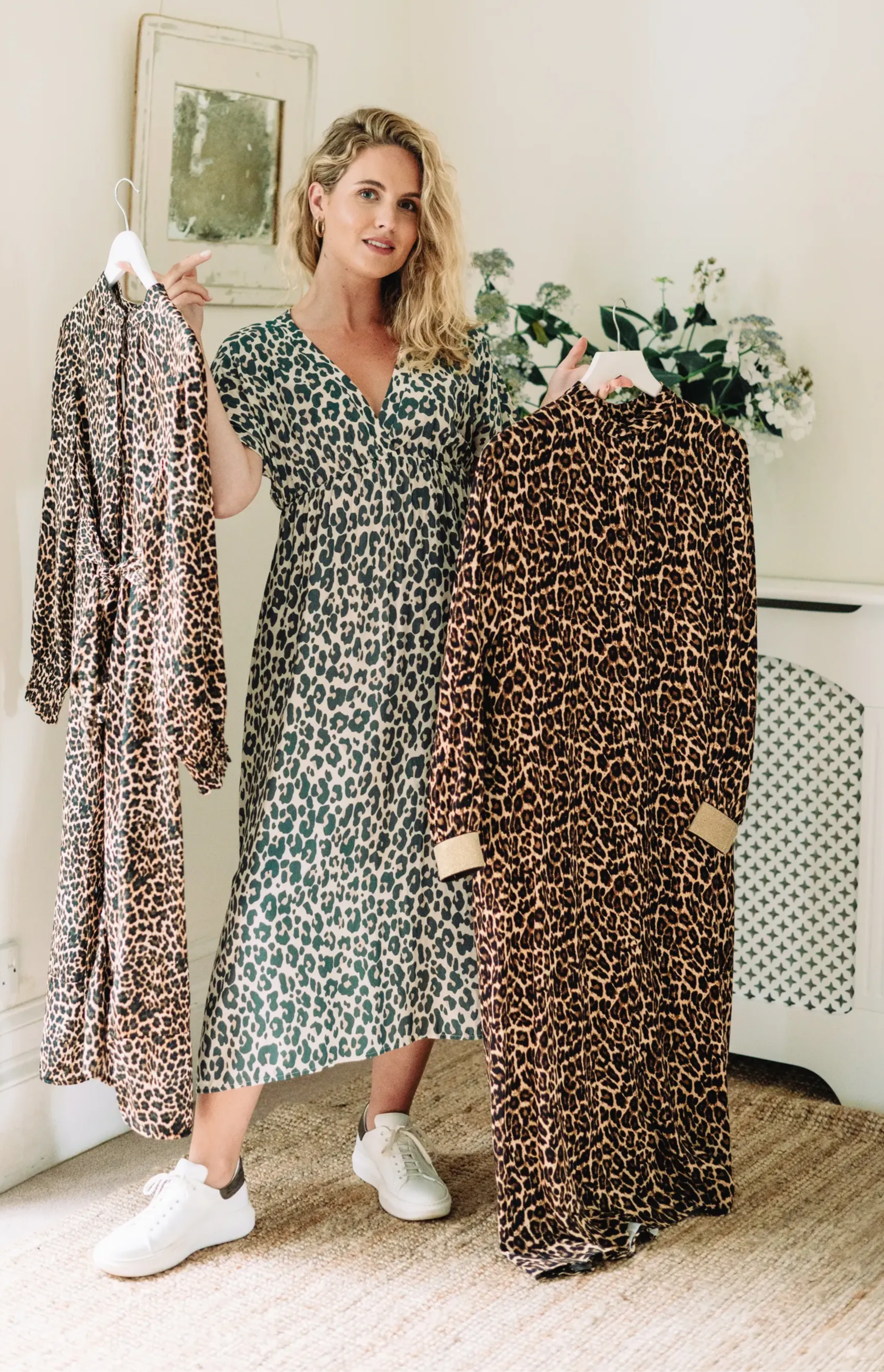 A model wearing a leopard print midi dress with short sleeves and white trainers holding two other leopard print dresses