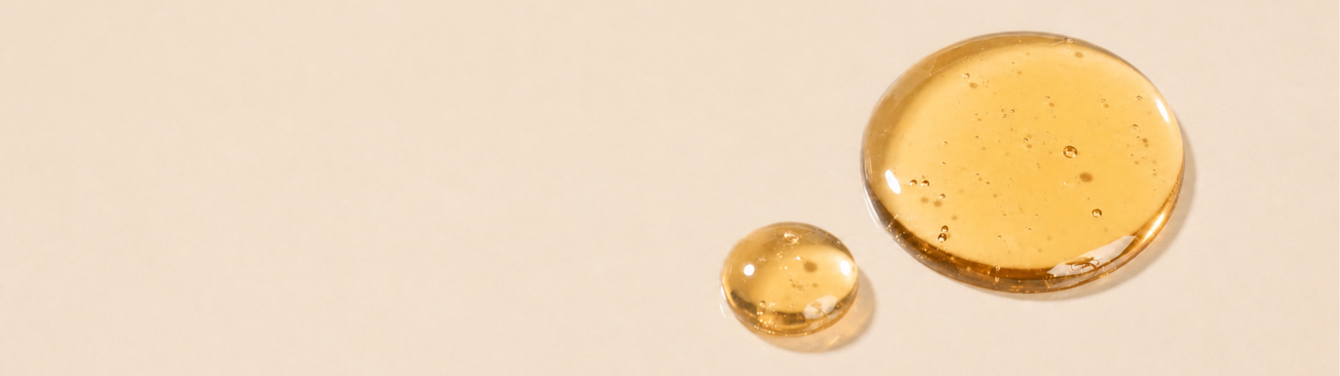 Two droplets of golden liquid on a beige background.