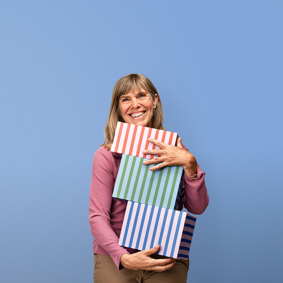 Smiling woman holding three striped gift boxes against a blue background.