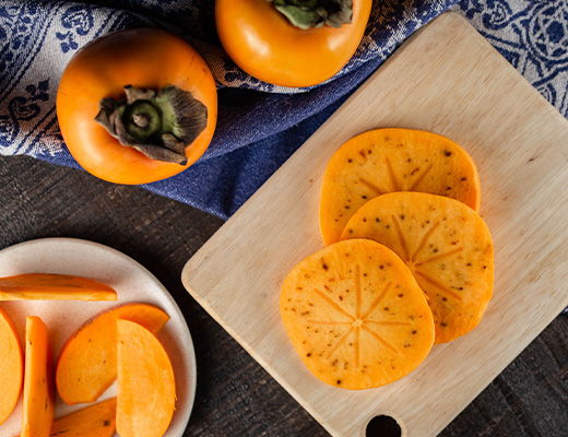 Sliced persimmons on a wooden board with whole fruit nearby.