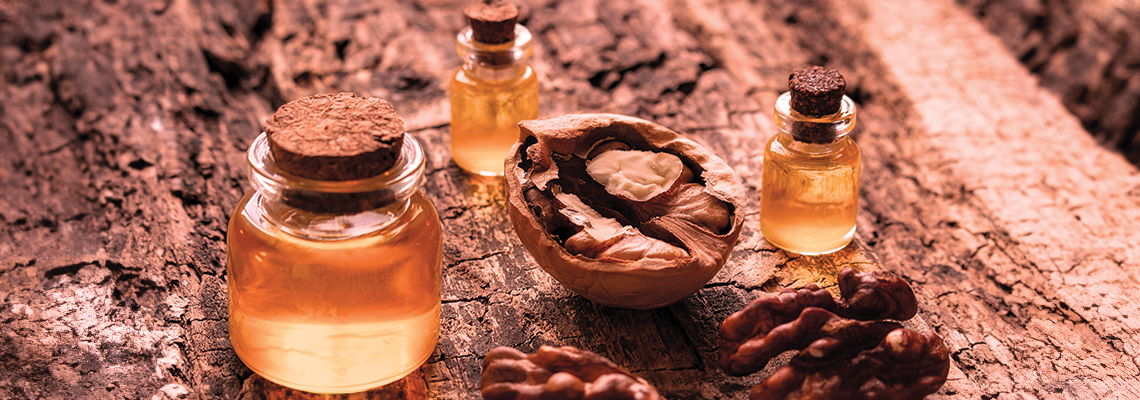 Glass jars of oil surrounded by nuts on a wooden surface.