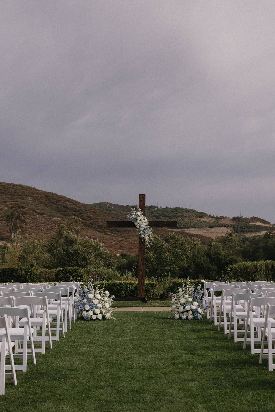 A wedding ceremony setup with chairs and a cross in a scenic landscape.