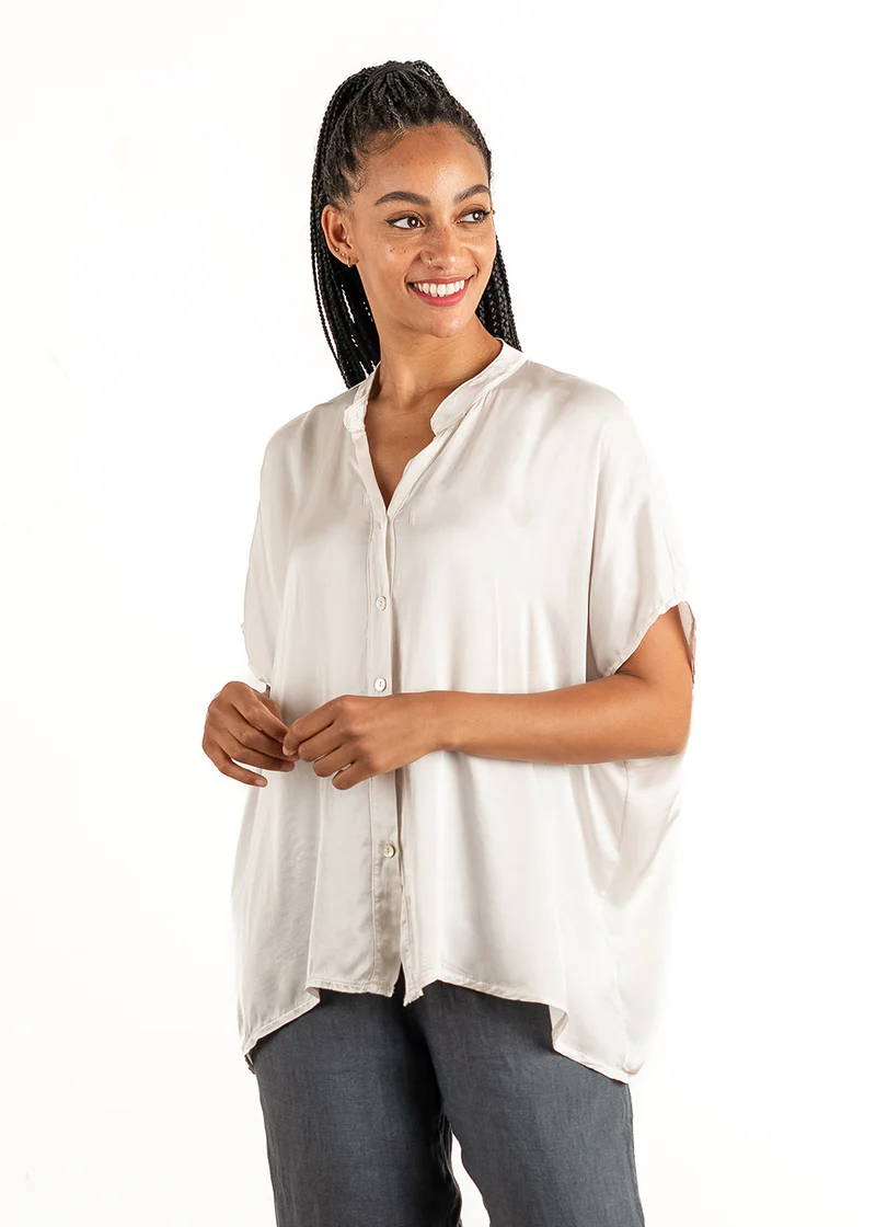 A model wearing an off white, boxy satin shirt with mid length sleeves