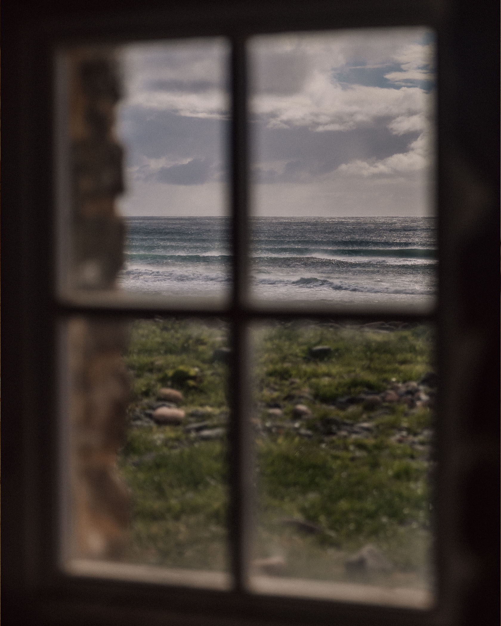 Blurred view of ocean and grassy shore through a rustic window.
