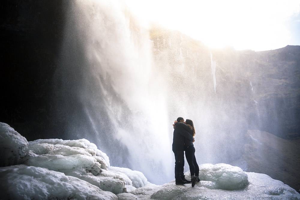 couple hugging underneath waterfall in iceland