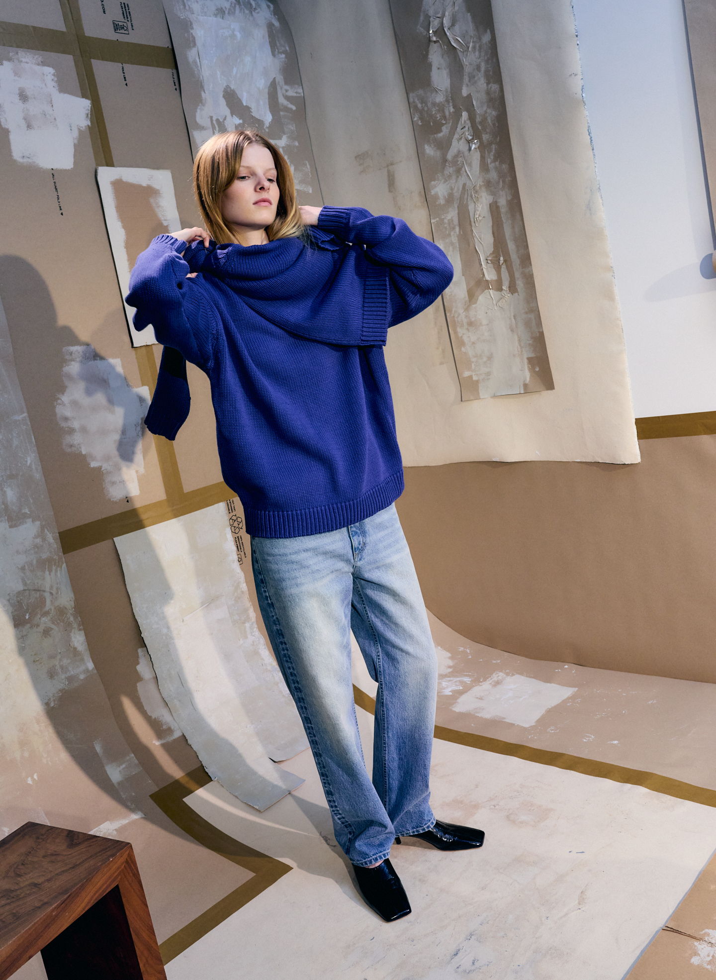 Person in a blue sweater and jeans in a styled indoor setting.