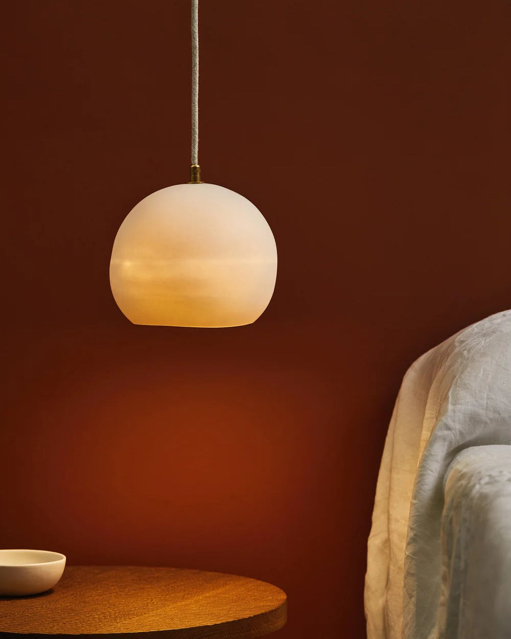 Spherical pendant light hanging against a red-brown wall with a textured surface.