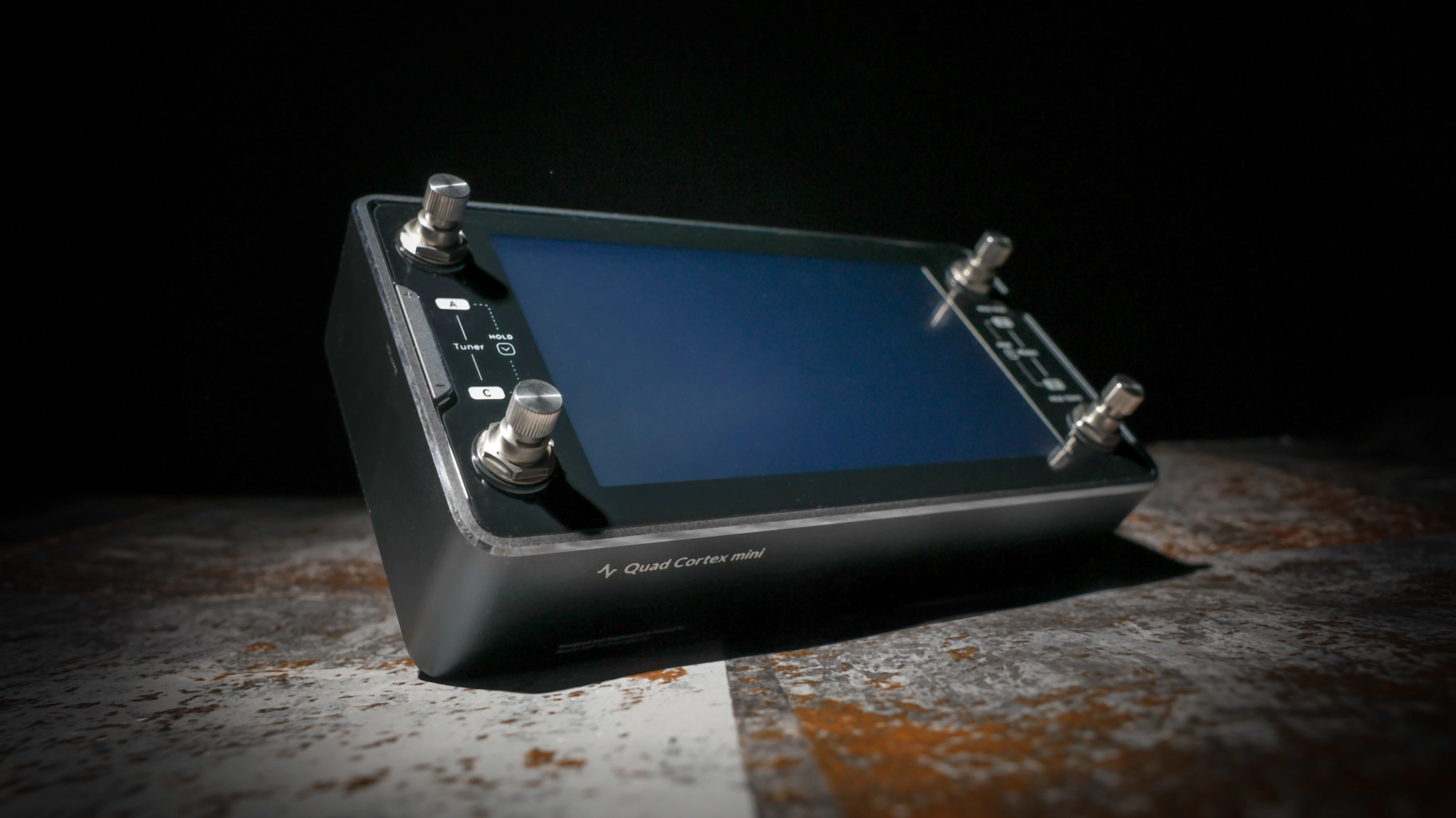 A Neural DSP Quad Cortex Mini with a screen and knobs, positioned on a surface.