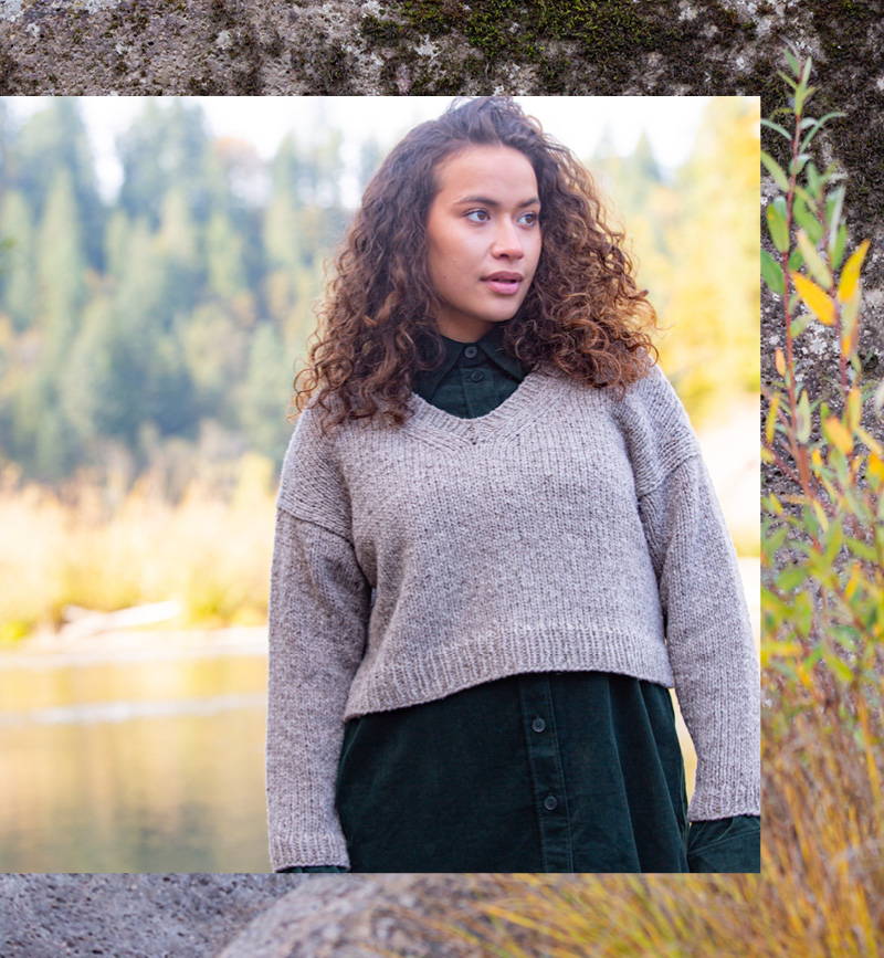 A female model with long curly hair wears the Lodge Pullover by Jared Flood in Quarry Woodsmoke.