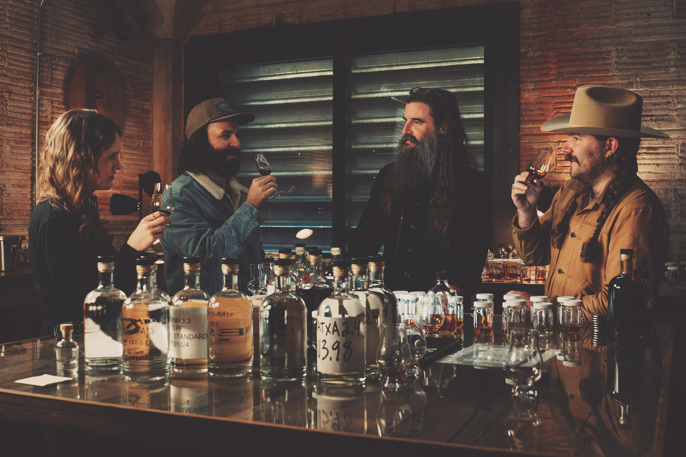 Four people in a bar discussing drinks with bottles on the counter.