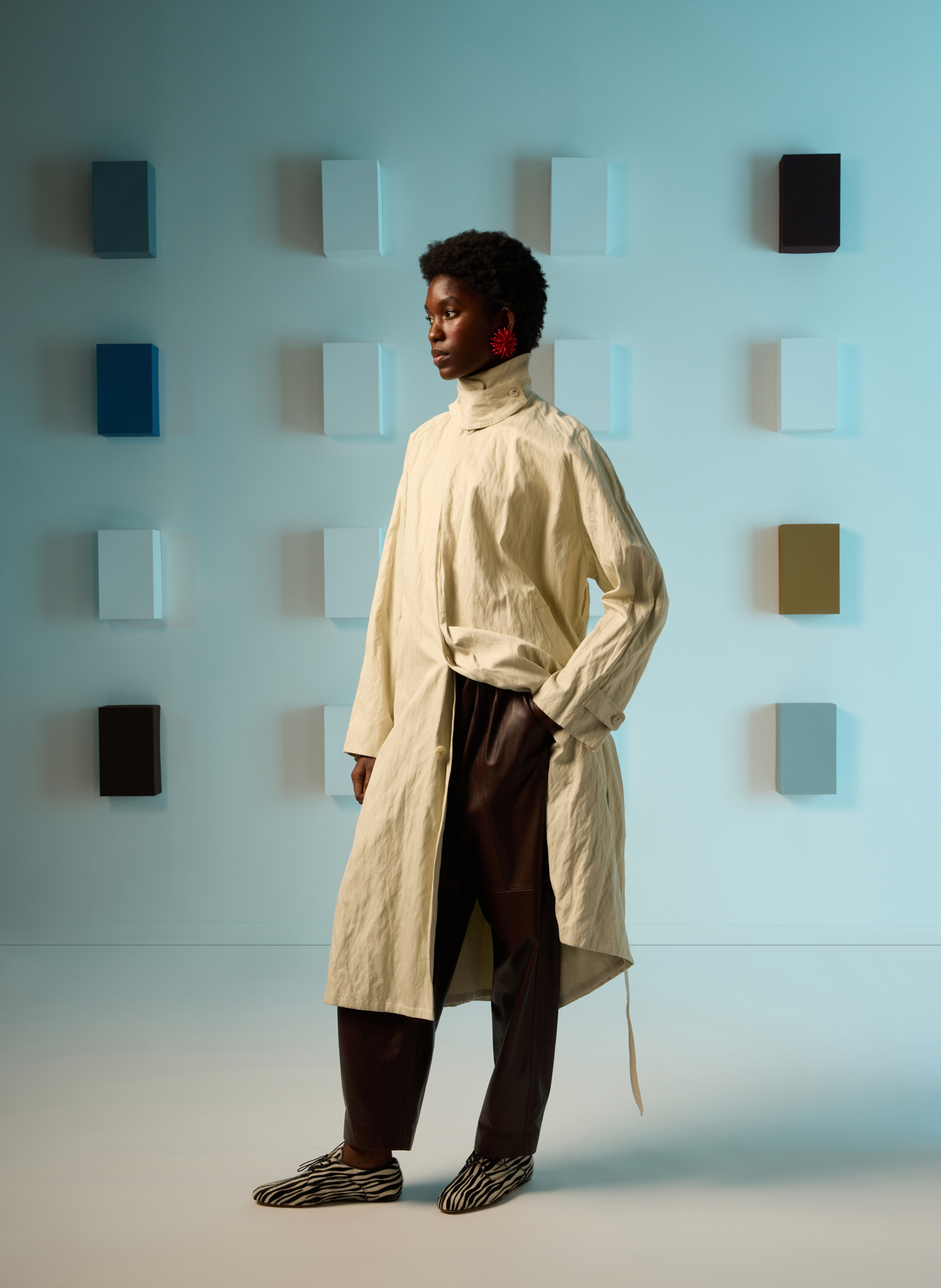 A person in a beige coat stands against a colorful background.