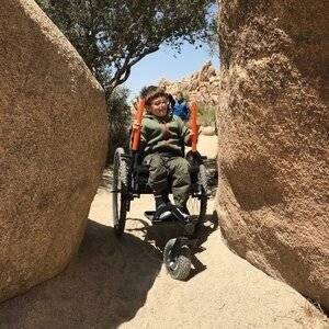 Child independently uses GRIT Freedom Chair all terrain wheelchair maneuvering between rock walls on dirt outdoors