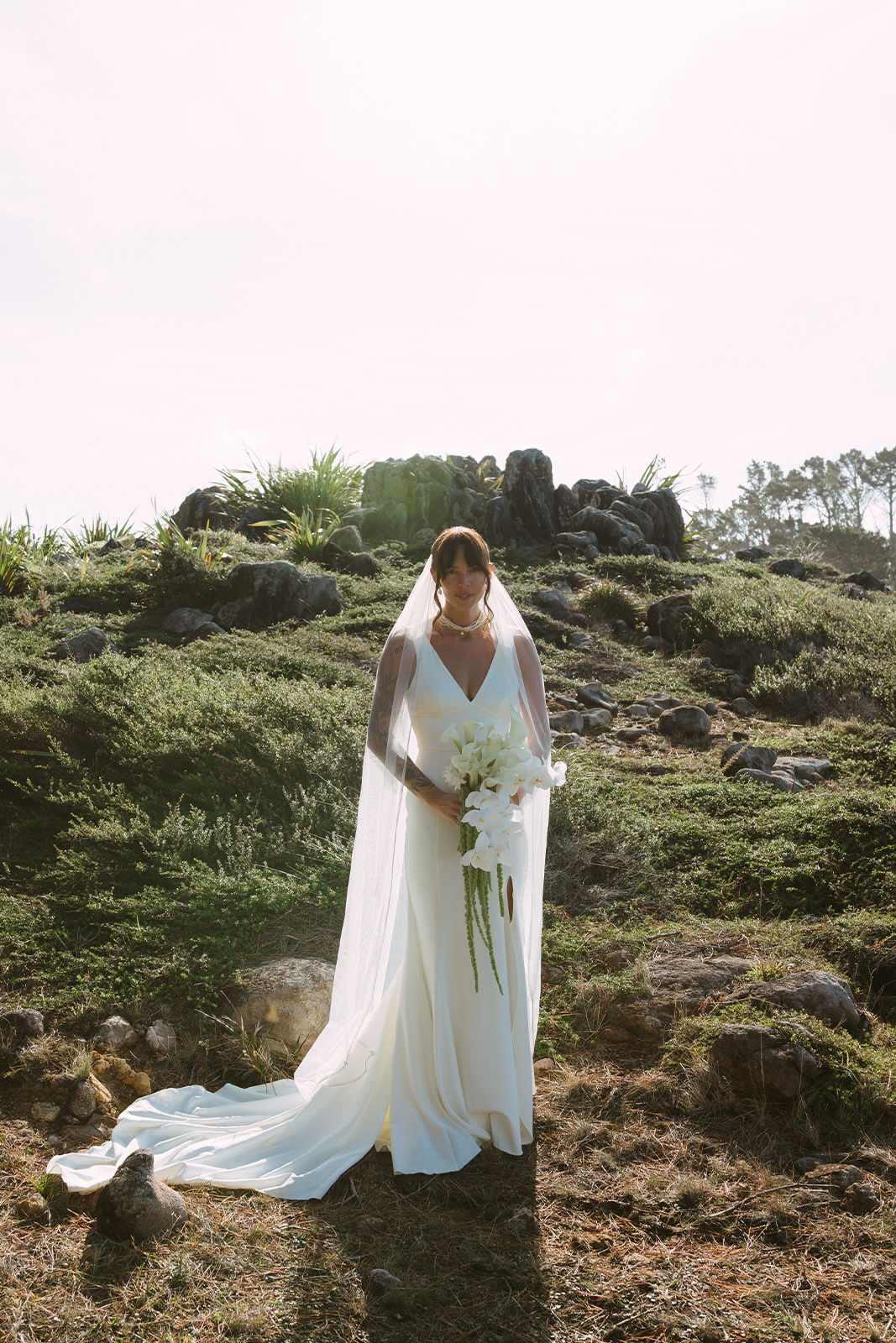 A bride in a white gown holding flowers in a natural setting.