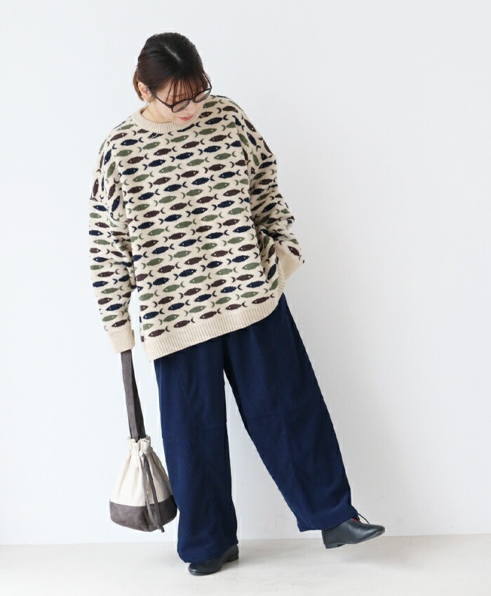 Person wearing a patterned sweater and dark pants, posing against a white background.