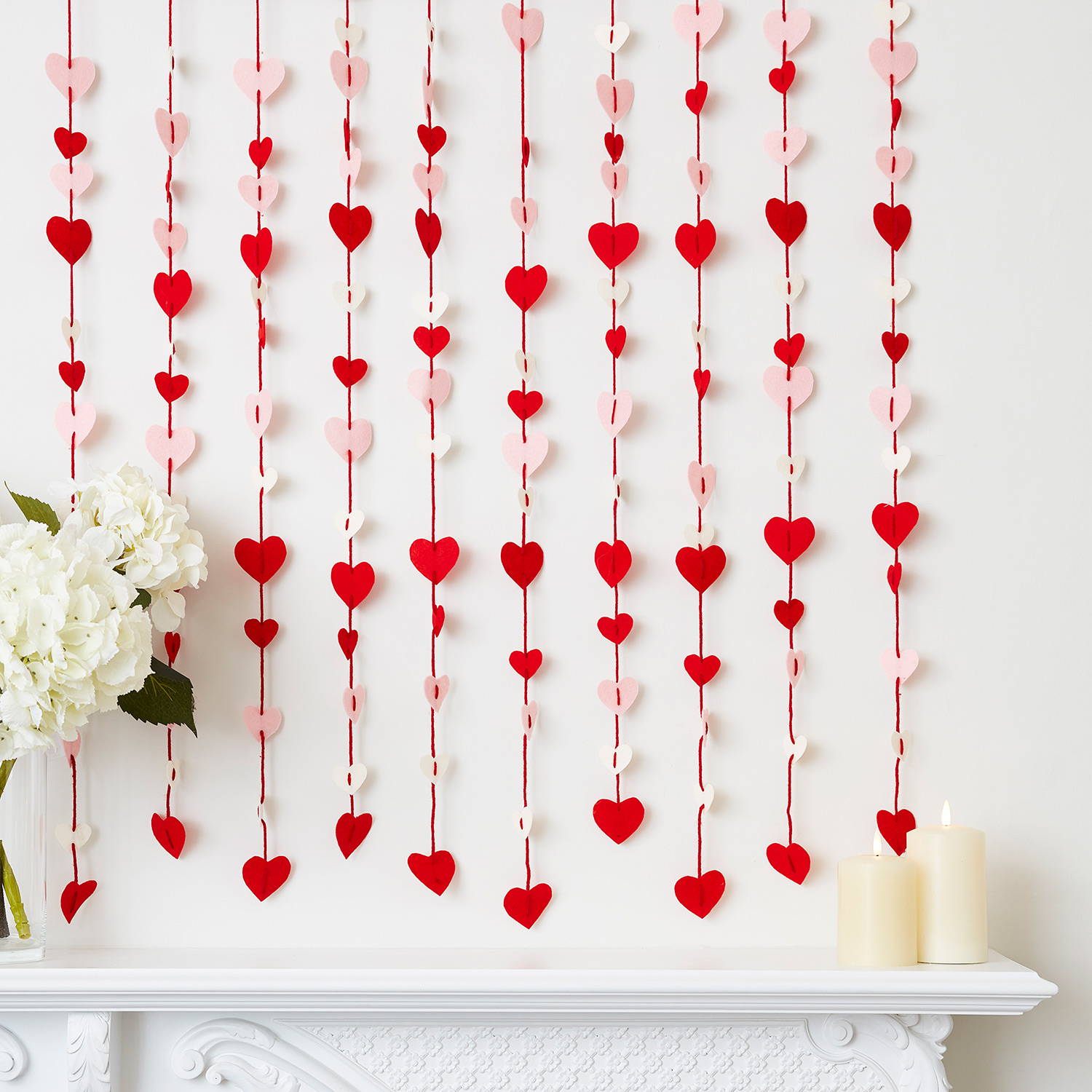 Red, pink and cream felt curtain over a mantlepiece with flowers and pillar candles.